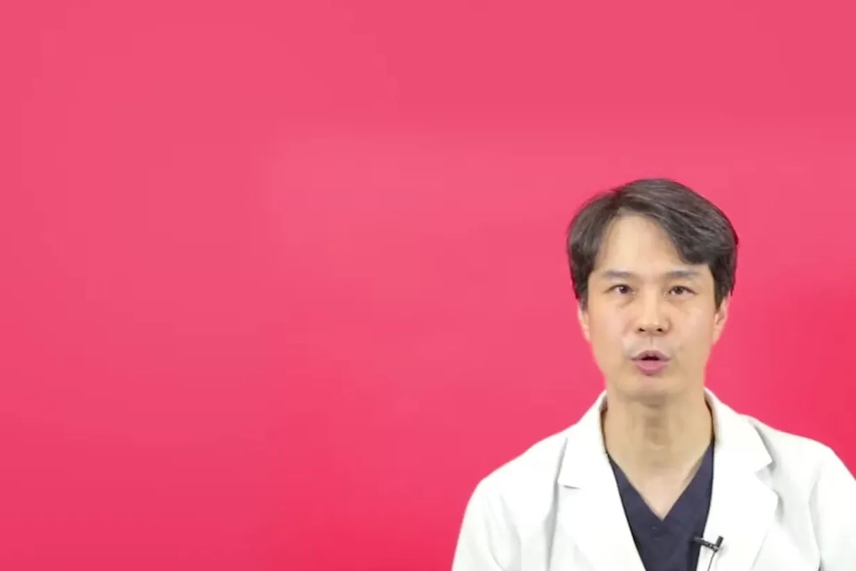 분홍 배경 앞에서 흰 가운을 입은 의사가 설명하는 모습