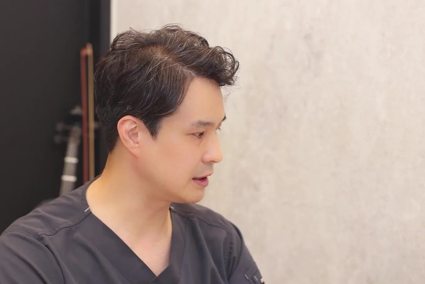 스크럽을 입은 의사가 상담실에서 옆을 보며 말하는 모습
