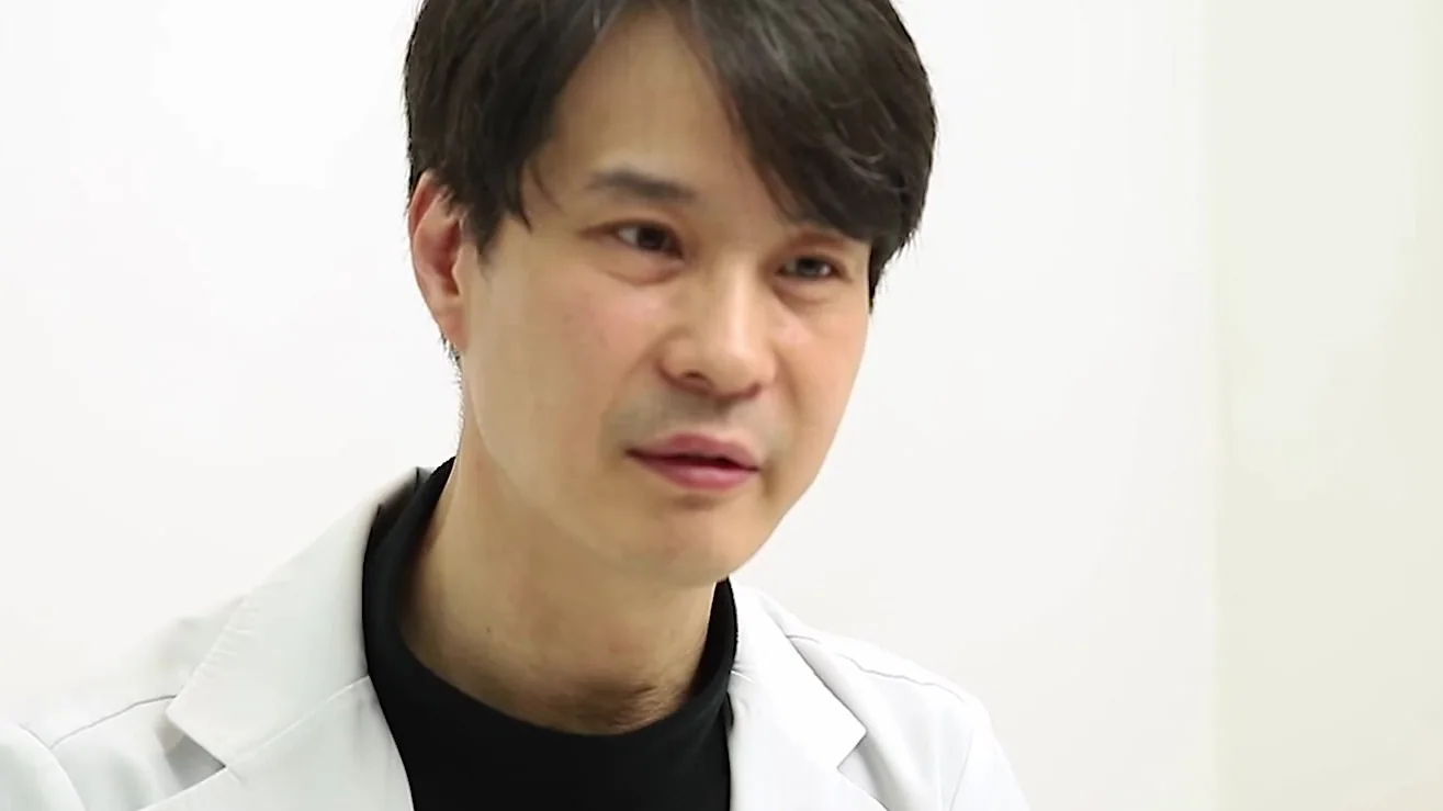 흰 가운을 입은 의사가 비스듬히 앉아 설명하는 모습