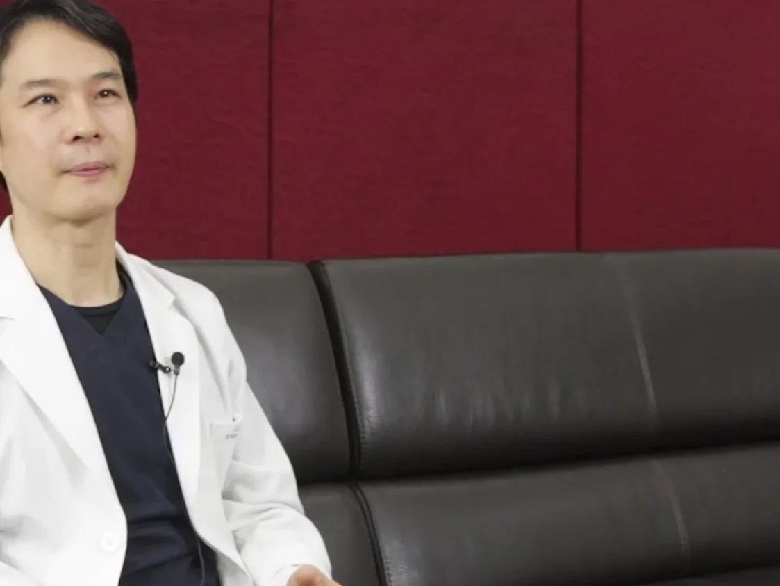 흰 가운을 입은 의사가 검은 가죽 소파에 앉아 있는 모습