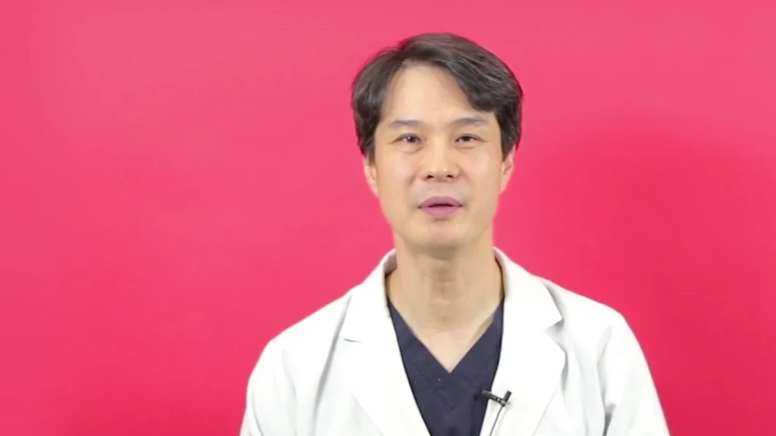 분홍 배경 앞에서 흰 가운을 입은 의사가 설명하는 모습